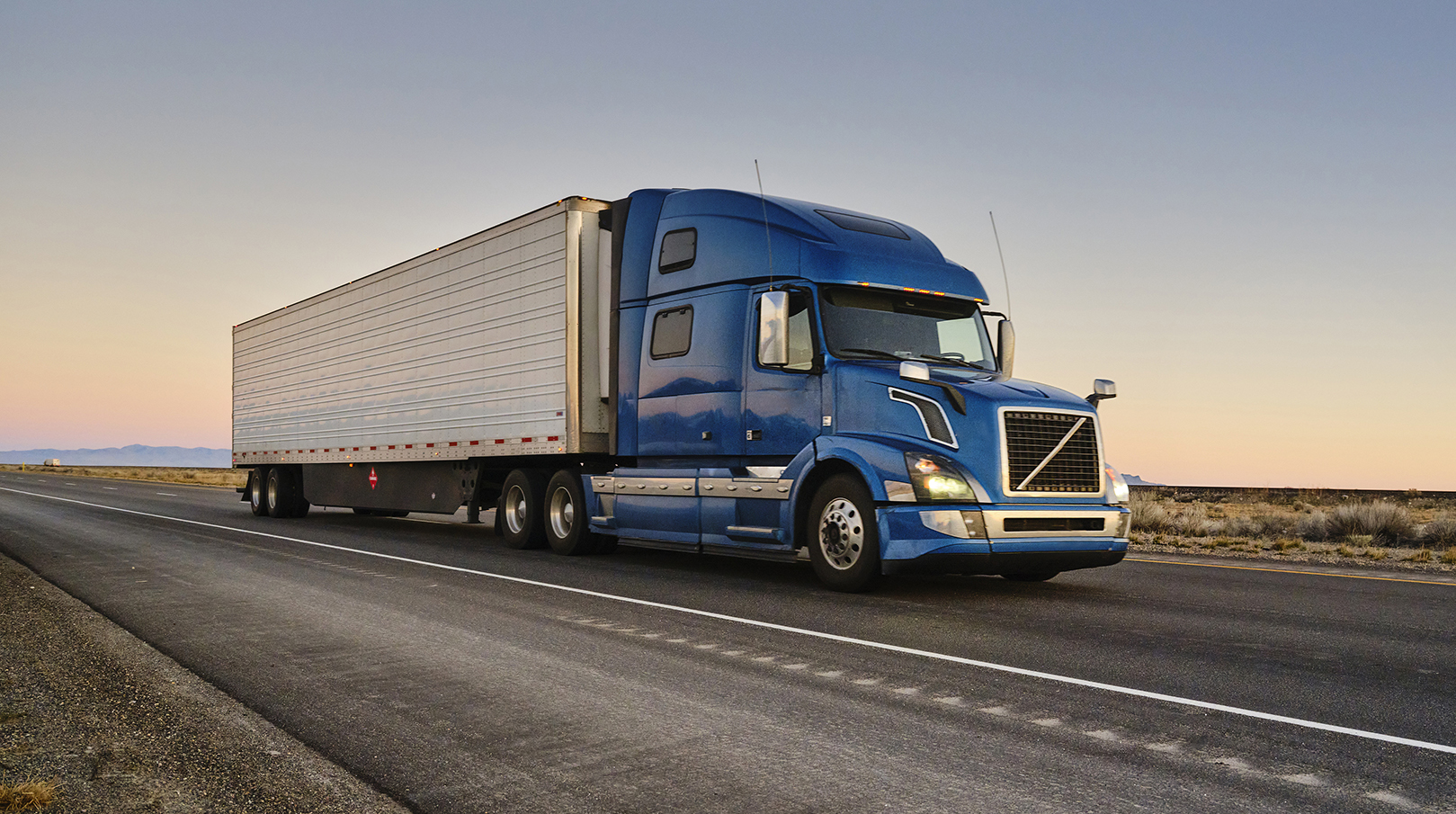A blue tractor-trailer drives along a highway