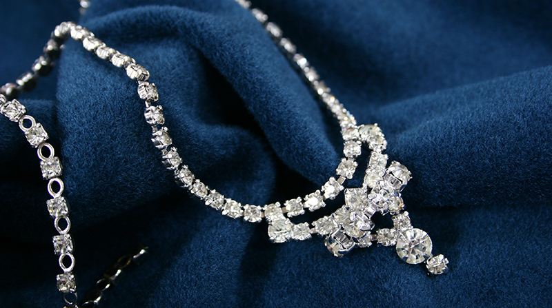 A vintage diamond necklace is draped on a navy velour fabric