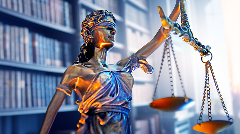 A sculpture of Lady Justice stands prominently, set against a backdrop of an elegant bookcase filled with legal volumes