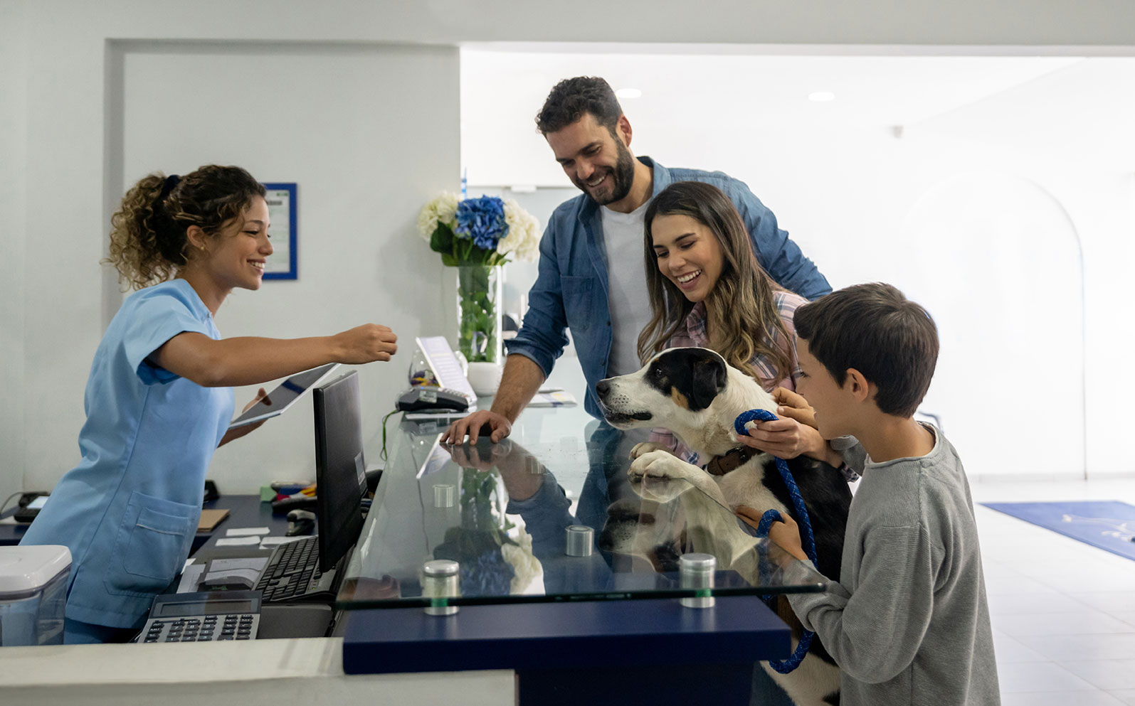 A happy family stands with their dog at the front desk of a veterinarian's office