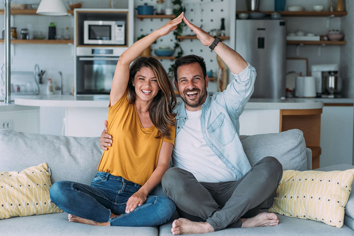 a happy couple makes a roof figure with their arms in their living room